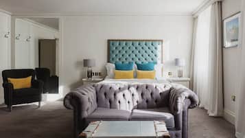 A bedroom with a tufted headboard, a grey upholstered sofa, a black armchair, and a bedside table with lamps.