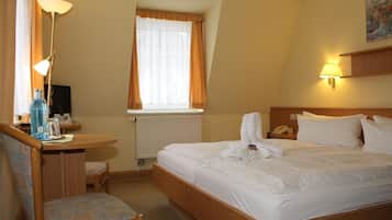 A hotel room with a bed, a desk with a chair, a lamp, a window with curtains, and a painting on the wall.