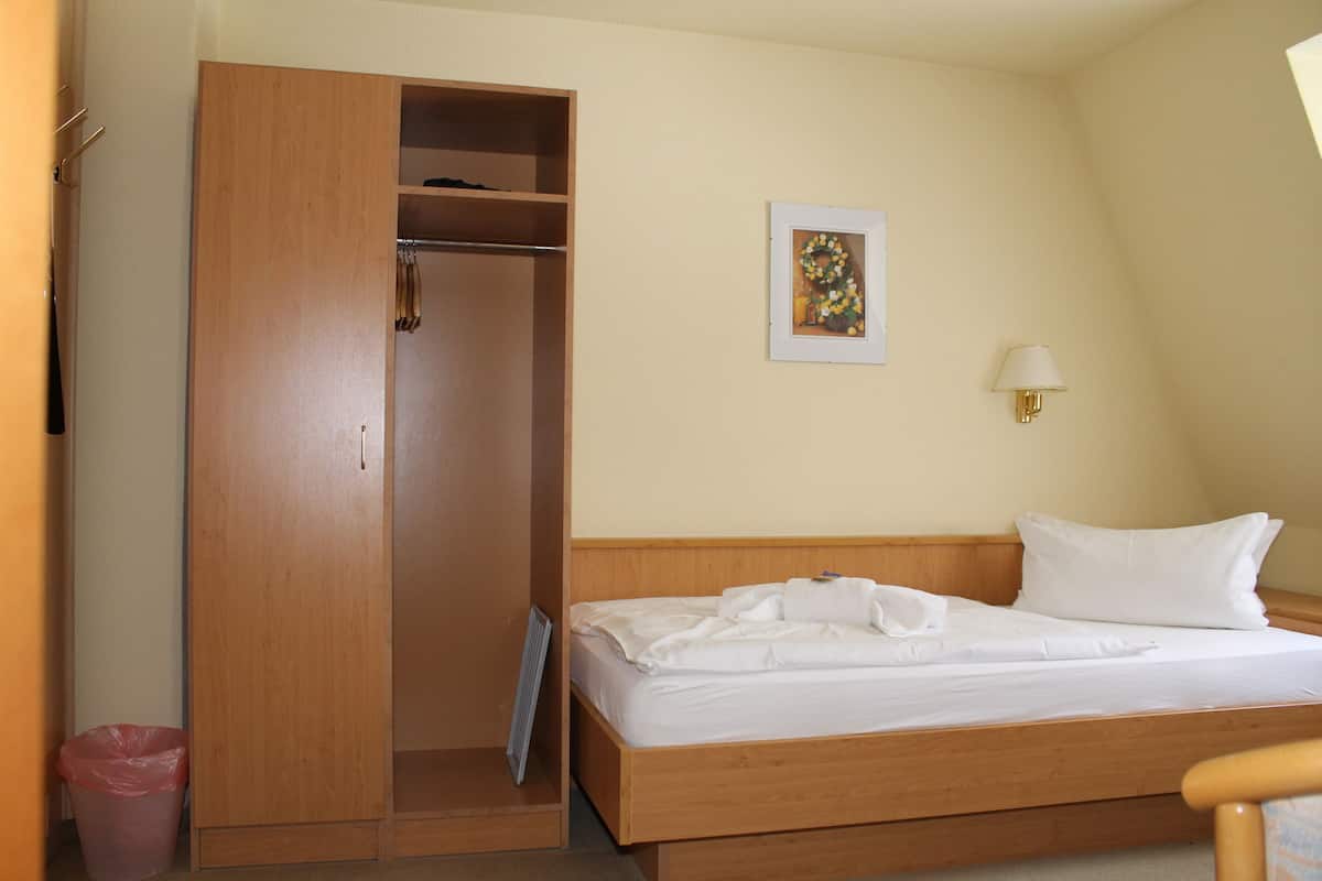 A bedroom with a wooden bed, a wooden wardrobe, a framed picture on the wall, and a bedside lamp.