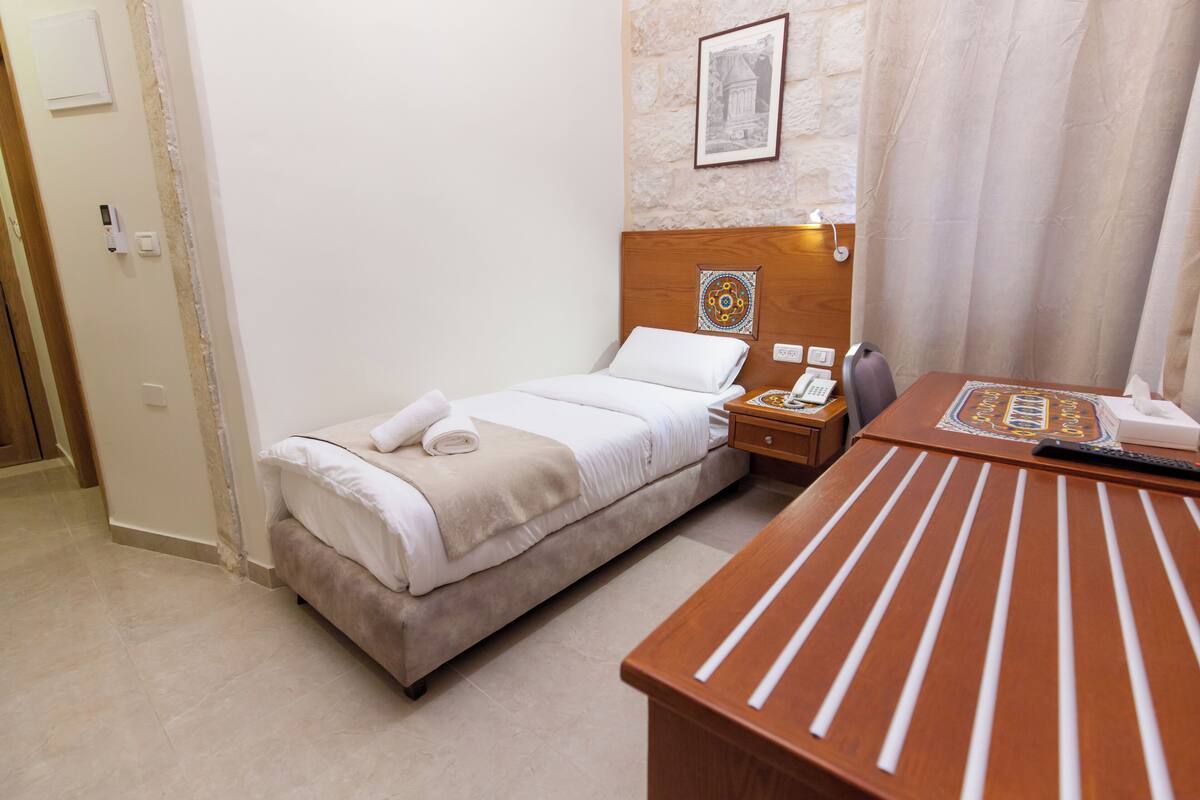 Quarto de hotel com cama, mesa de cabeceira e secretária com telefone.
