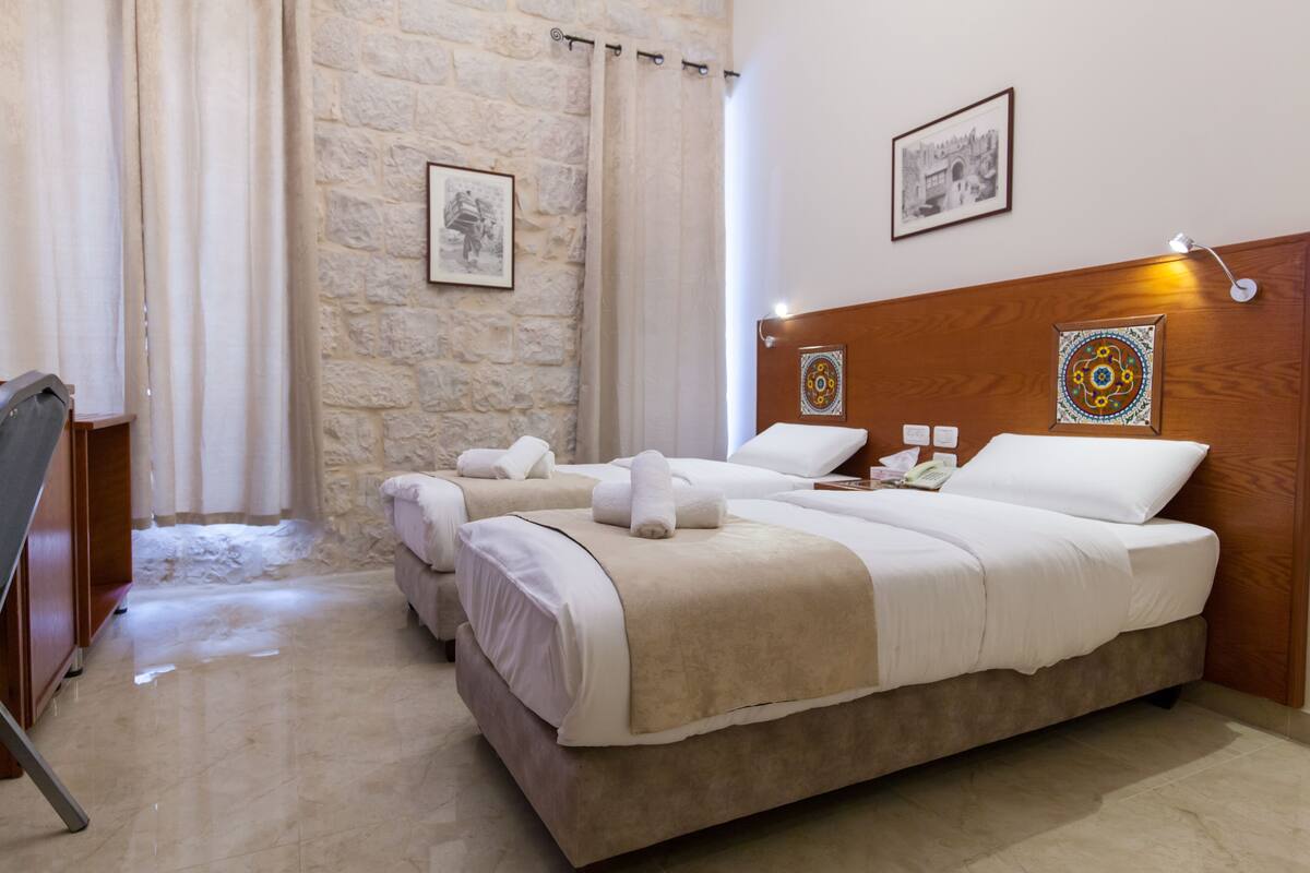 Quarto de hotel com duas camas, uma parede de pedra e uma cabeceira de madeira.