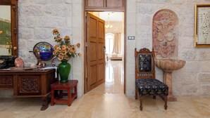 A hallway with a wooden door, a green vase with flowers, a wooden chair, and a stone wall. - Azzahra Boutique Hotel & Restaurant - Jerusalem (Jerusalem)
