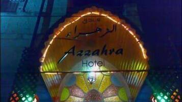 Das Außengelände des Hotels Az Zahrat mit beleuchteter Beschilderung und dekorativer Beleuchtung.
