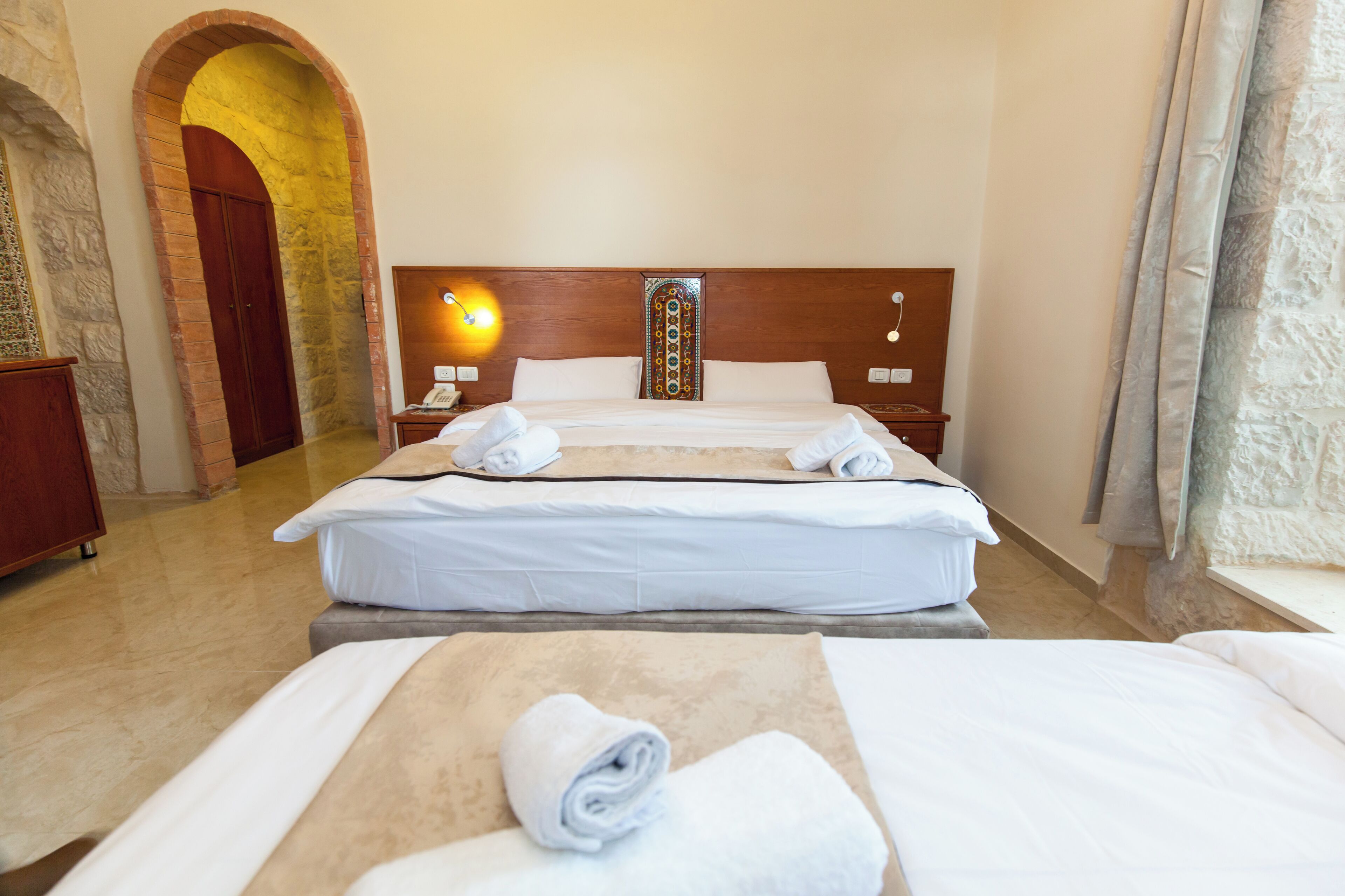 Une chambre d’hôtel avec deux lits, une tête de lit en bois, une arche en pierre et une table de chevet avec une lampe.