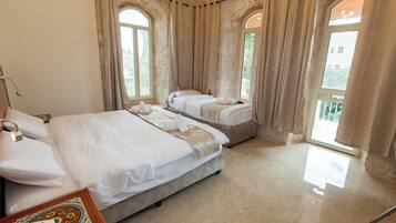 A hotel room with two beds, a wooden nightstand with a telephone, and large windows with curtains.