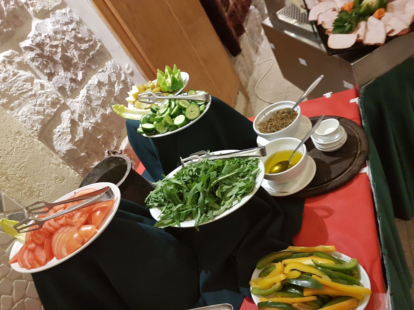 Een tafel met diverse gerechten, waaronder komkommerschijfjes, tomaten, bladgroenten en paprika.