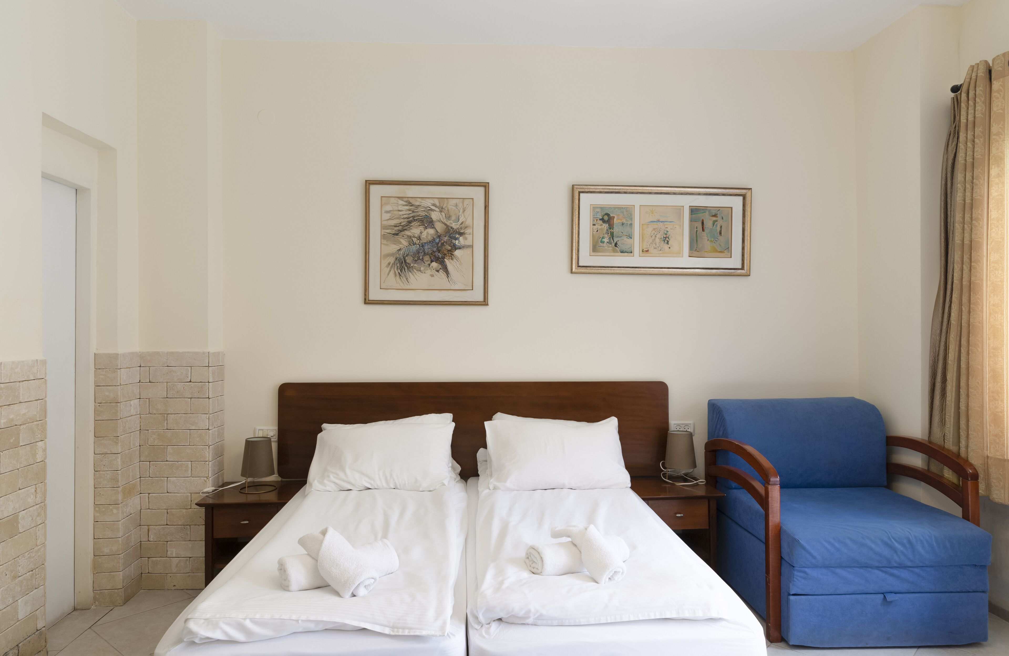 A hotel room with two beds, a blue chair, and artwork on the walls.