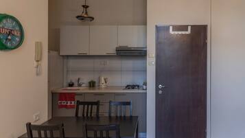A compact kitchen with white cabinets, a dining table with chairs, a clock, and a door.