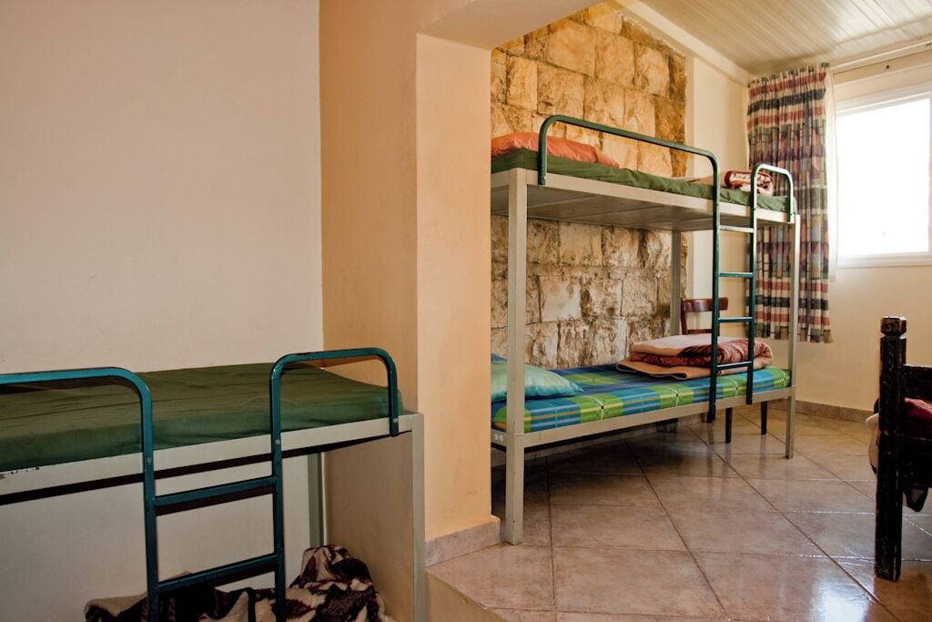 A dormitory room with bunk beds, a stone wall, and a window with curtains.
