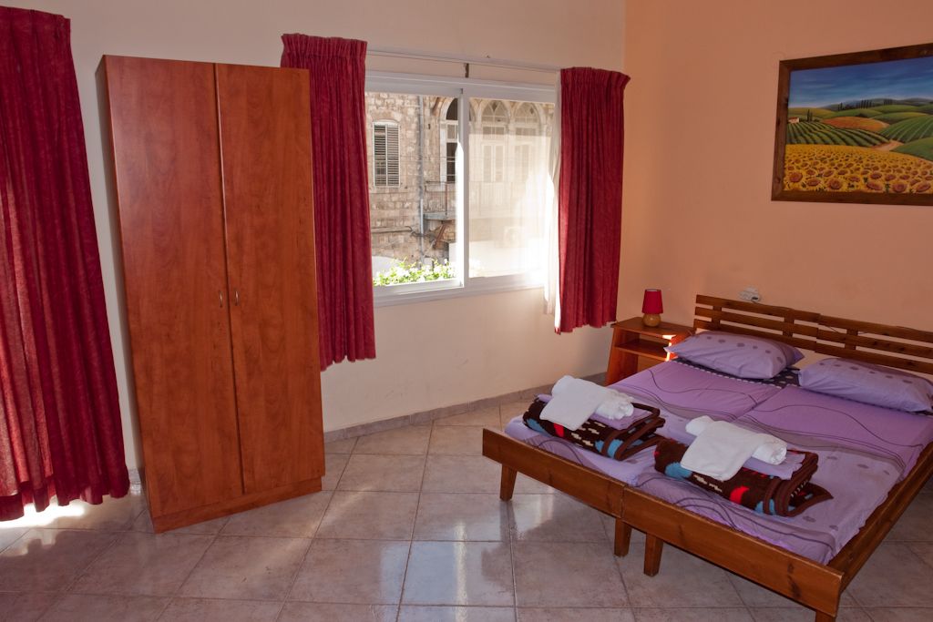 Un dormitorio con cama de madera, mesita de noche, armario y ventana con cortinas.