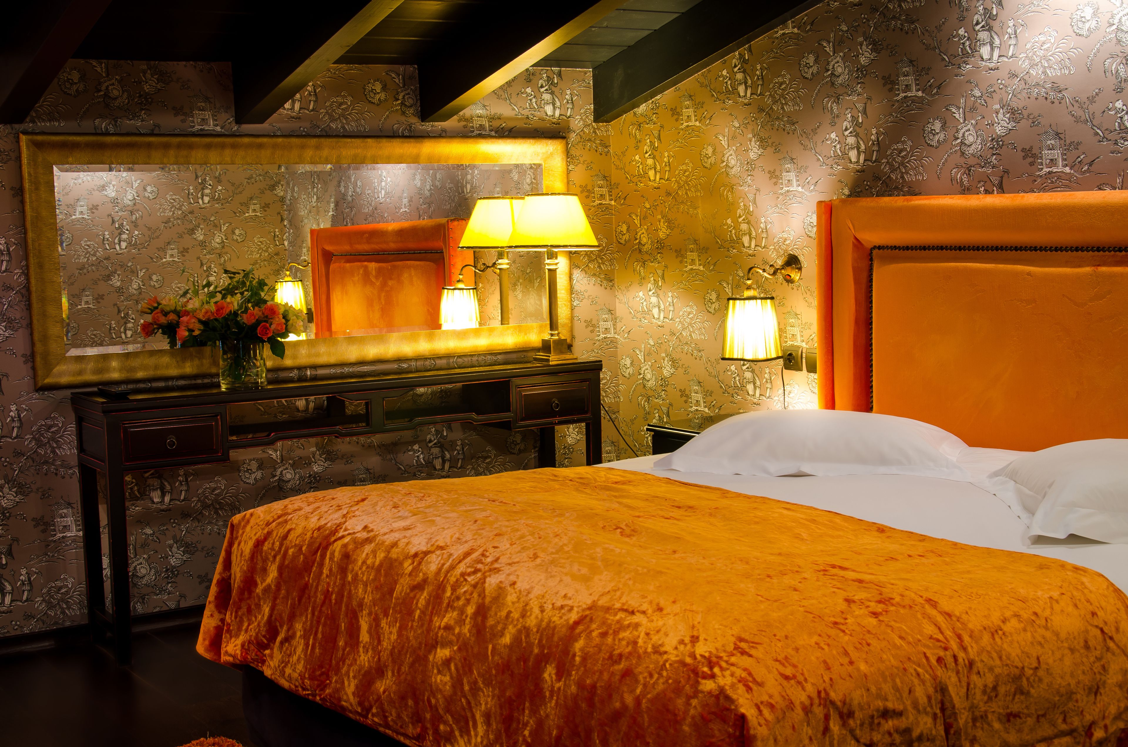 A hotel room with a large bed, a dresser with a mirror, and two wall-mounted lamps.