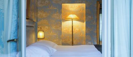 Habitación de hotel con cama, mesita de noche con lámpara y pared con papel tapiz estampado.