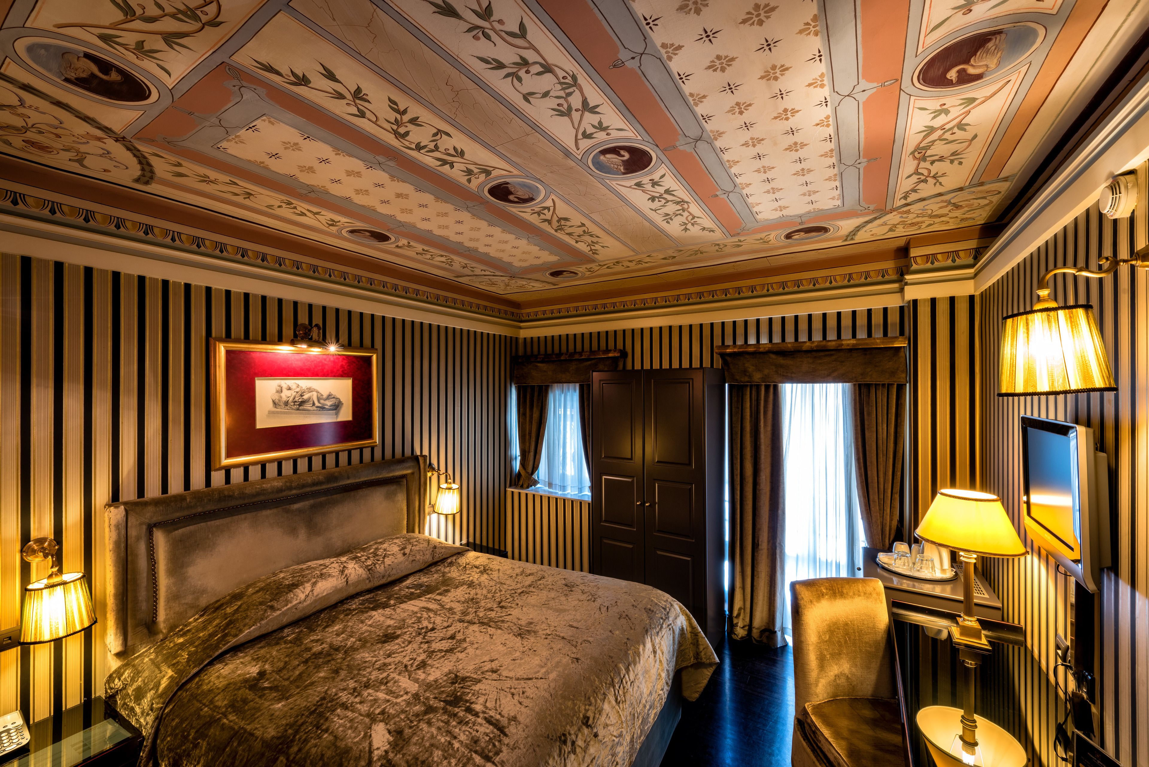 Ein Hotelzimmer mit einem großen Bett, einem Schreibtisch mit Lampe, einem Fernseher und einem gerahmten Bild an der Wand.