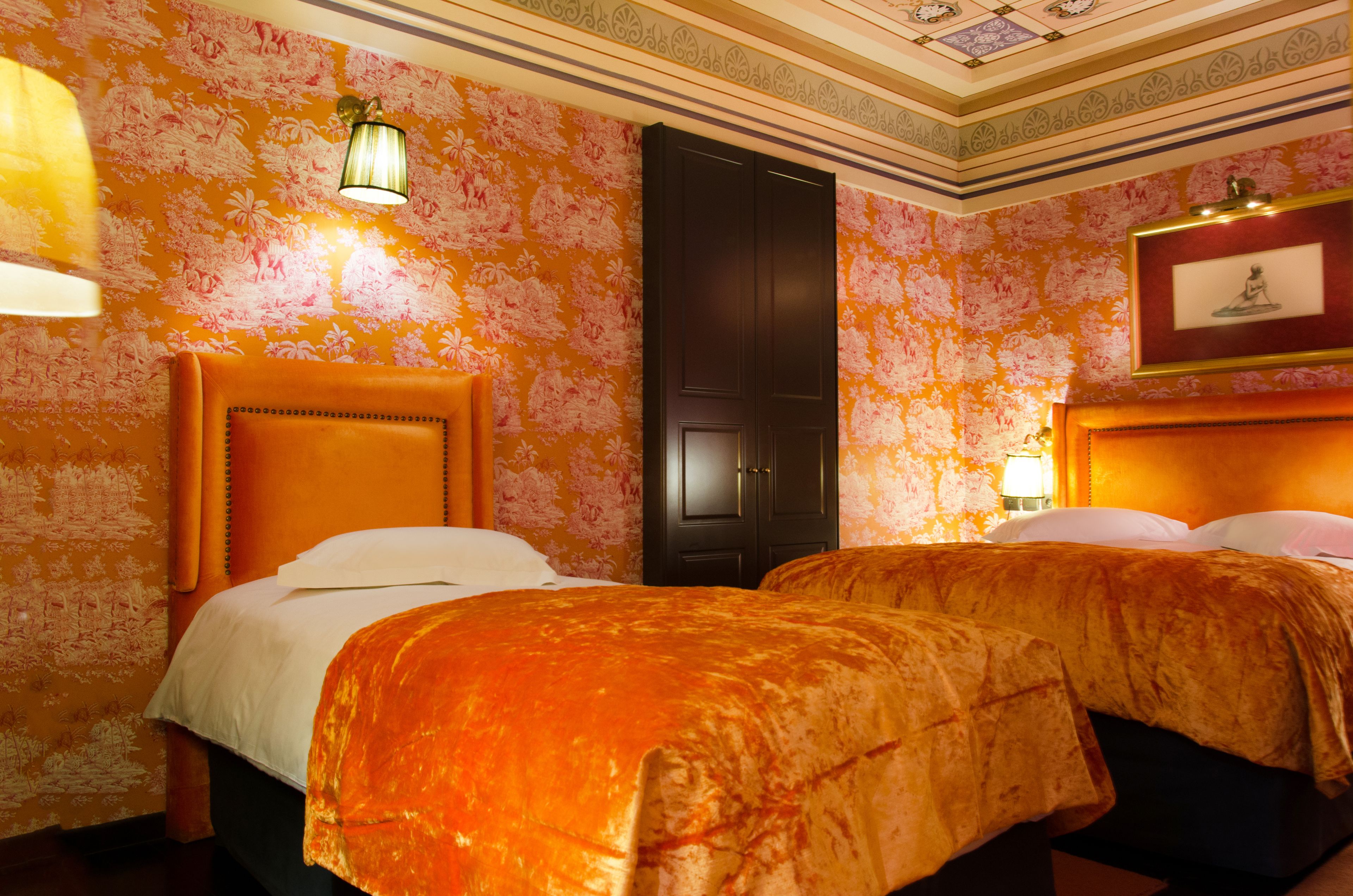 Habitación de hotel con dos camas, un cabecero de madera grande, papel tapiz floral y un cuadro en la pared.