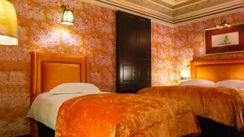 Habitación de hotel con dos camas, un cabecero de madera grande, papel tapiz floral y un cuadro en la pared.