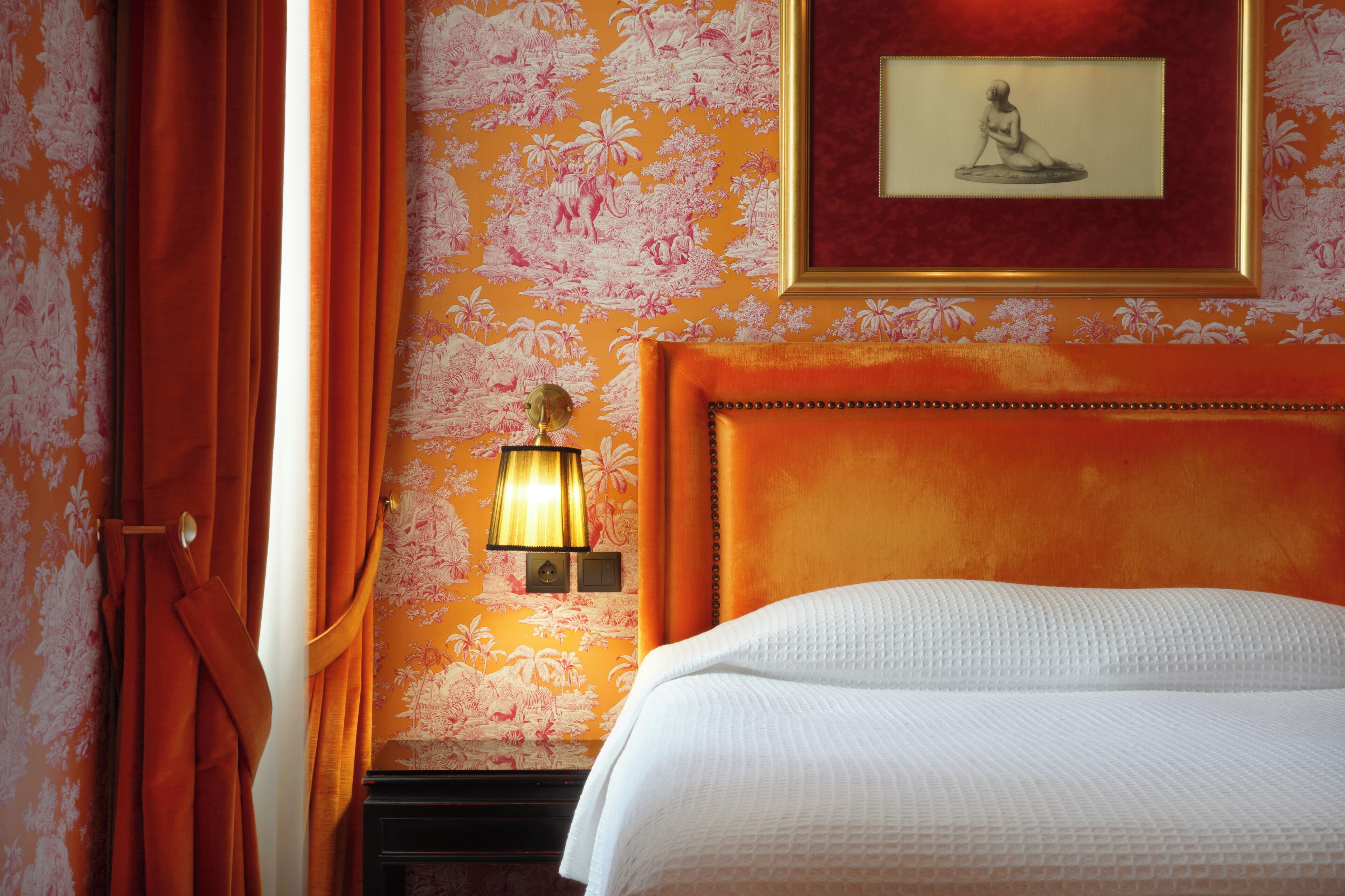 A hotel room with a bed, a nightstand, a lamp, and a framed picture on the wall.