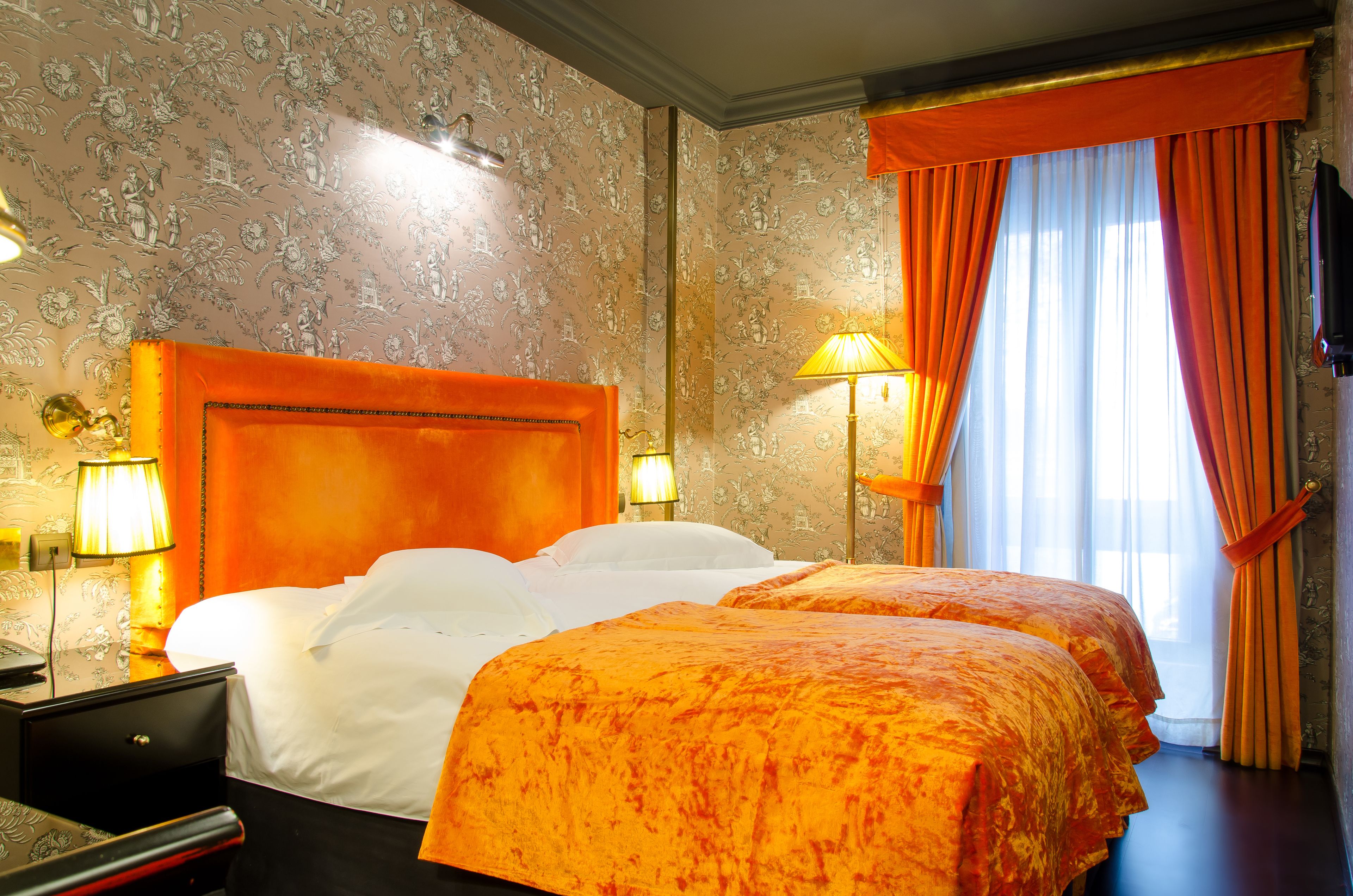 A hotel room with a large bed, two bedside tables, and a window with curtains.