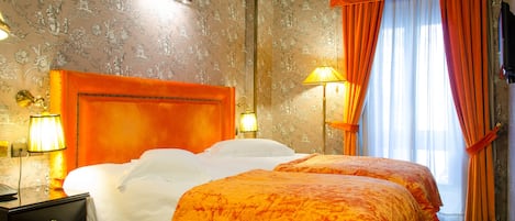 A hotel room with a large bed, two bedside tables, and a window with curtains.