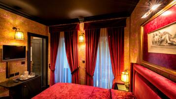 Een hotelkamer met een rode plaid, een bureau met een lamp, een televisie en een ingelijst schilderij aan de muur.