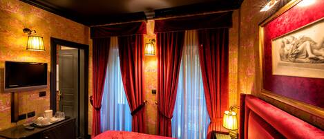 Una habitación de hotel con una colcha roja, un escritorio con lámpara, un televisor y un cuadro en la pared.