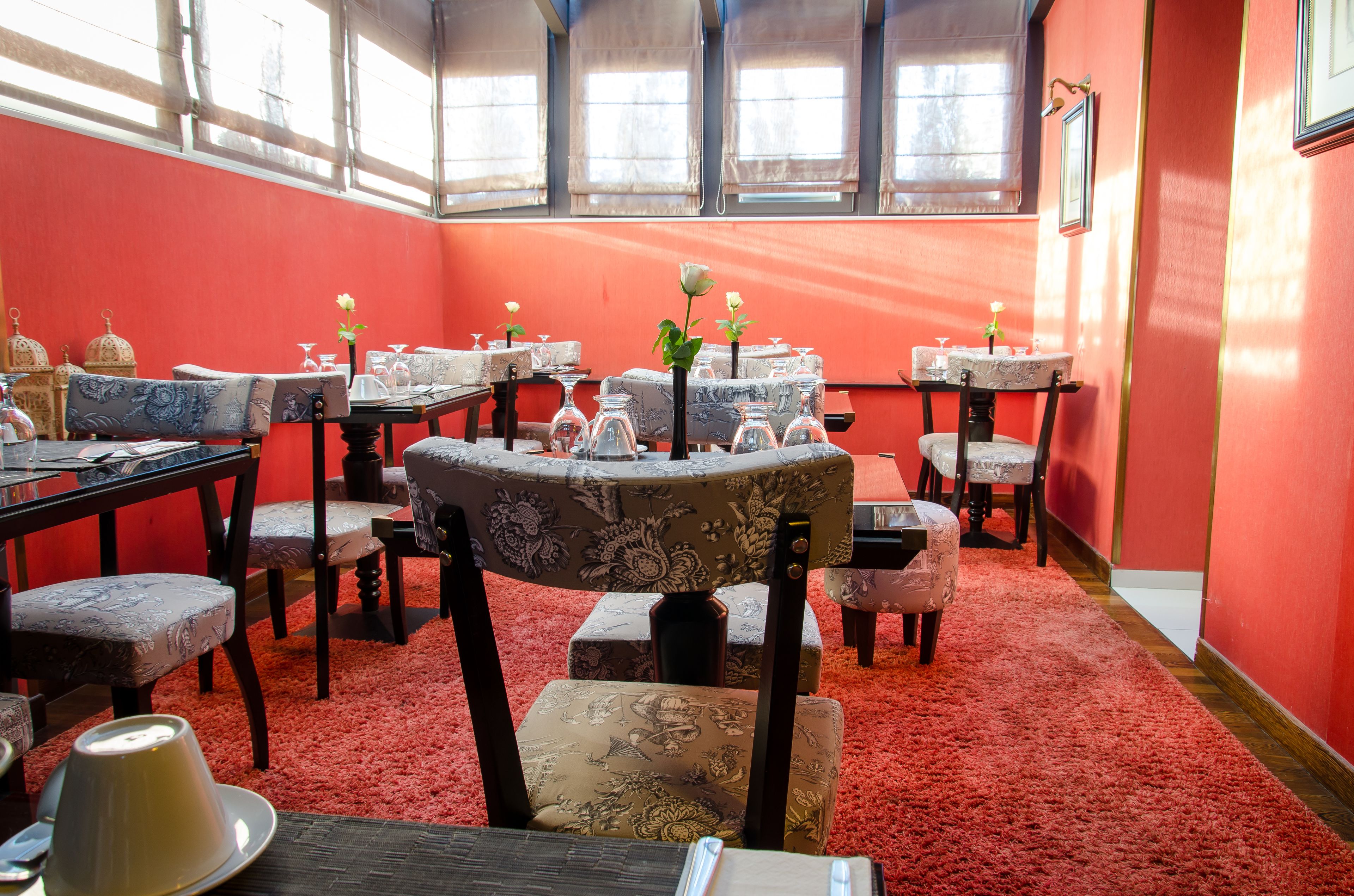 Un comedor con varias mesas y sillas, paredes rojas y ventanas amplias.