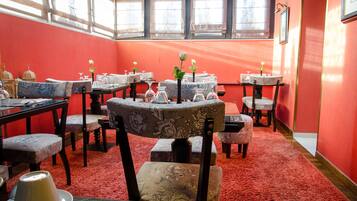 Un comedor con varias mesas y sillas, paredes rojas y ventanas amplias.