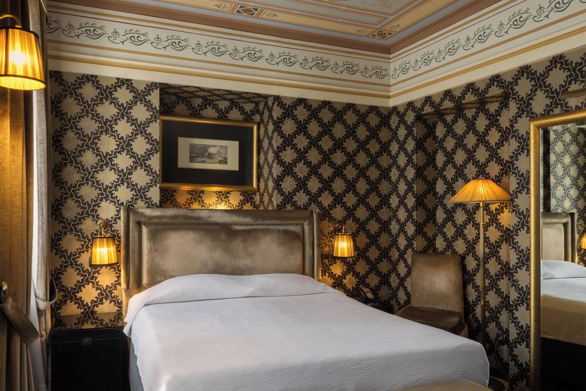 A hotel room with a large bed, two bedside lamps, a framed picture on the wall, and a mirror.
