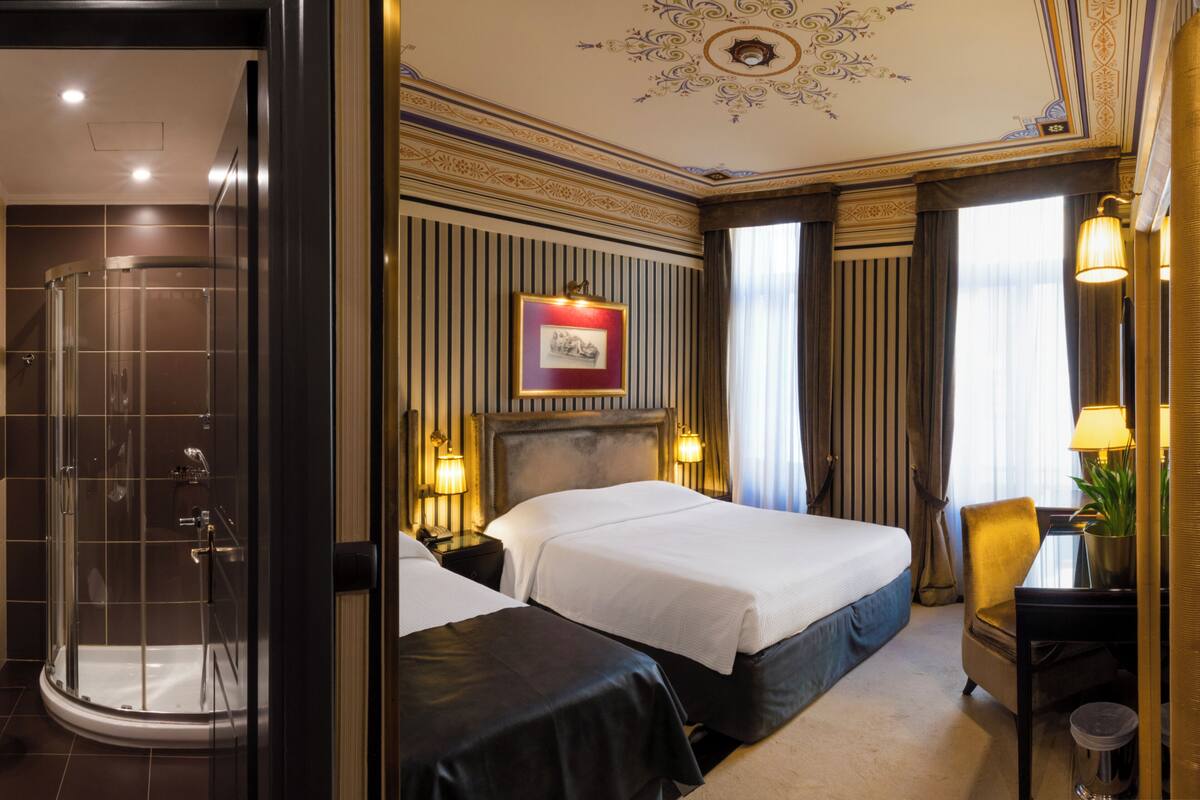 A hotel room with a large bed, a shower, a desk with a lamp, and a framed picture on the wall.