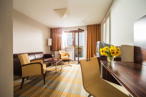 Una habitación de hotel con un sofá de cuero marrón, dos sillones, una mesa de centro de madera y un escritorio de madera con un jarrón de girasoles.