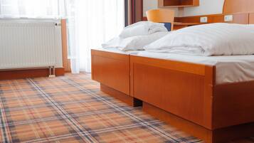 Ett hotellrum med ett rutigt golv, en säng med vita sängkläder, en sänggavel i trä, en spegel och ett element.