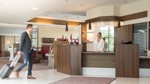 A modern reception area with a wooden reception desk, a seating area with red chairs, and a large window providing a view of the outdoors. - Hotel Liebmann (Lassnitzhoehe)