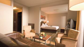 Habitación de hotel con cama, televisor, sofá, sillón y una mesita con fruta.