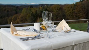A table set for dining with a scenic view of a forest and mountains in the background. - Hotel Liebmann (Lassnitzhoehe)