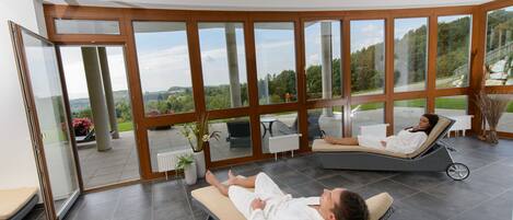 A modern spa area with two reclining chairs, a glass-enclosed patio, and a view of the surrounding landscape.