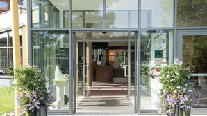 A modern hotel entrance with glass doors, a reception desk, and potted plants. - Hotel Liebmann (Lassnitzhoehe)