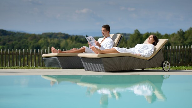 Two people relaxing on lounge chairs by a pool with a view of the mountains. - Hotel Liebmann (Lassnitzhoehe)