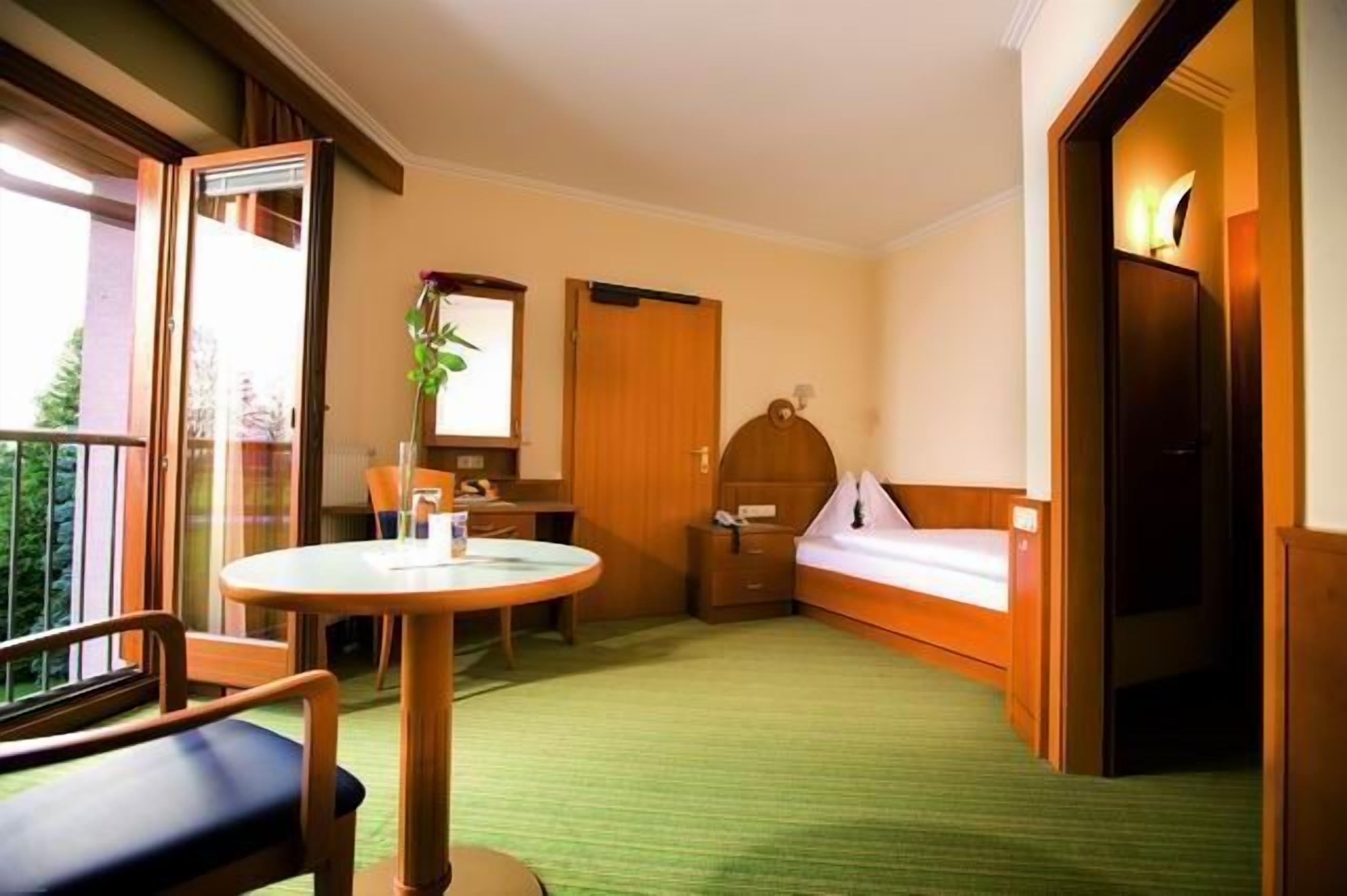 Ein Hotelzimmer mit Balkon, einem runden Tisch, einem Bett und einem Schreibtisch.