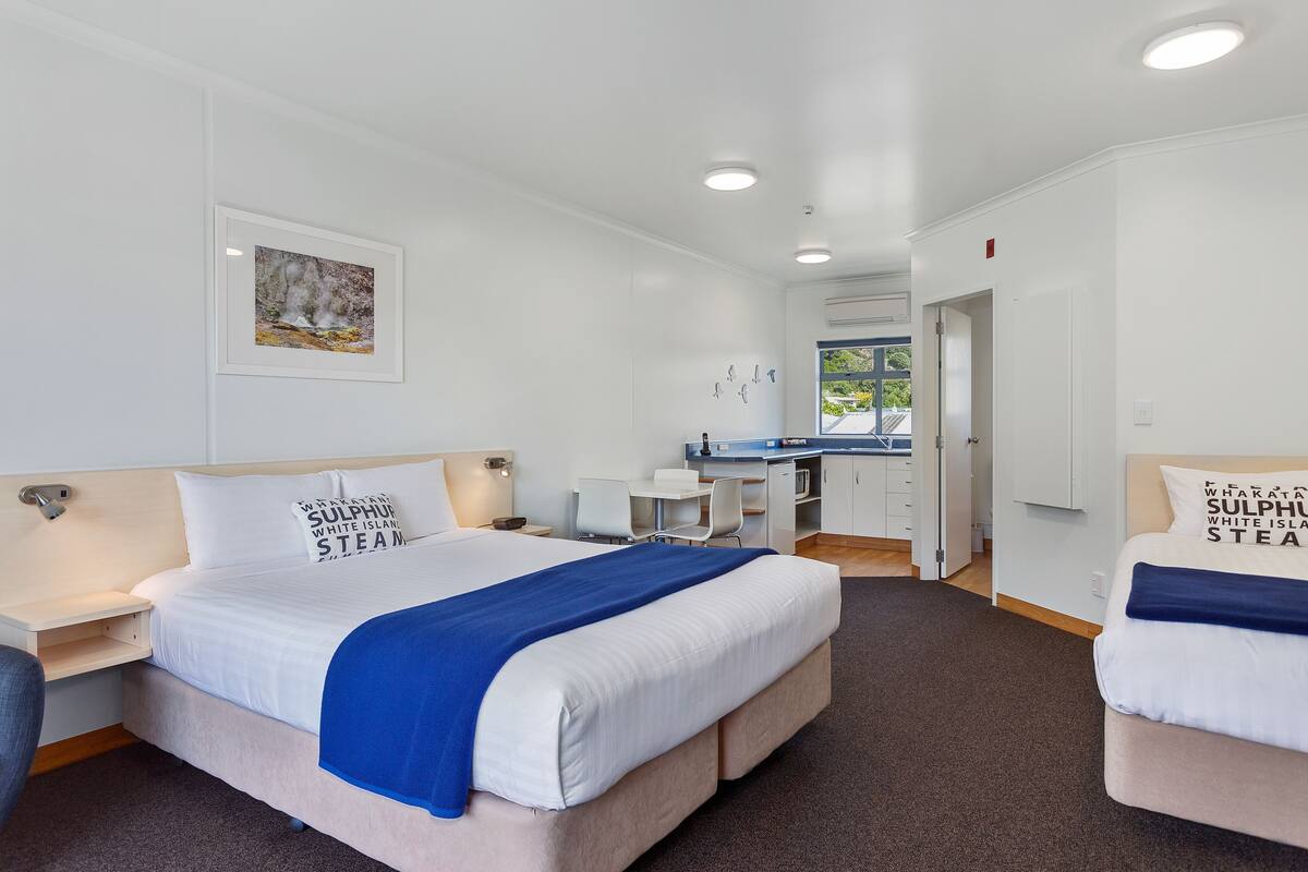 A hotel room with a large bed, a desk, and a kitchenette.