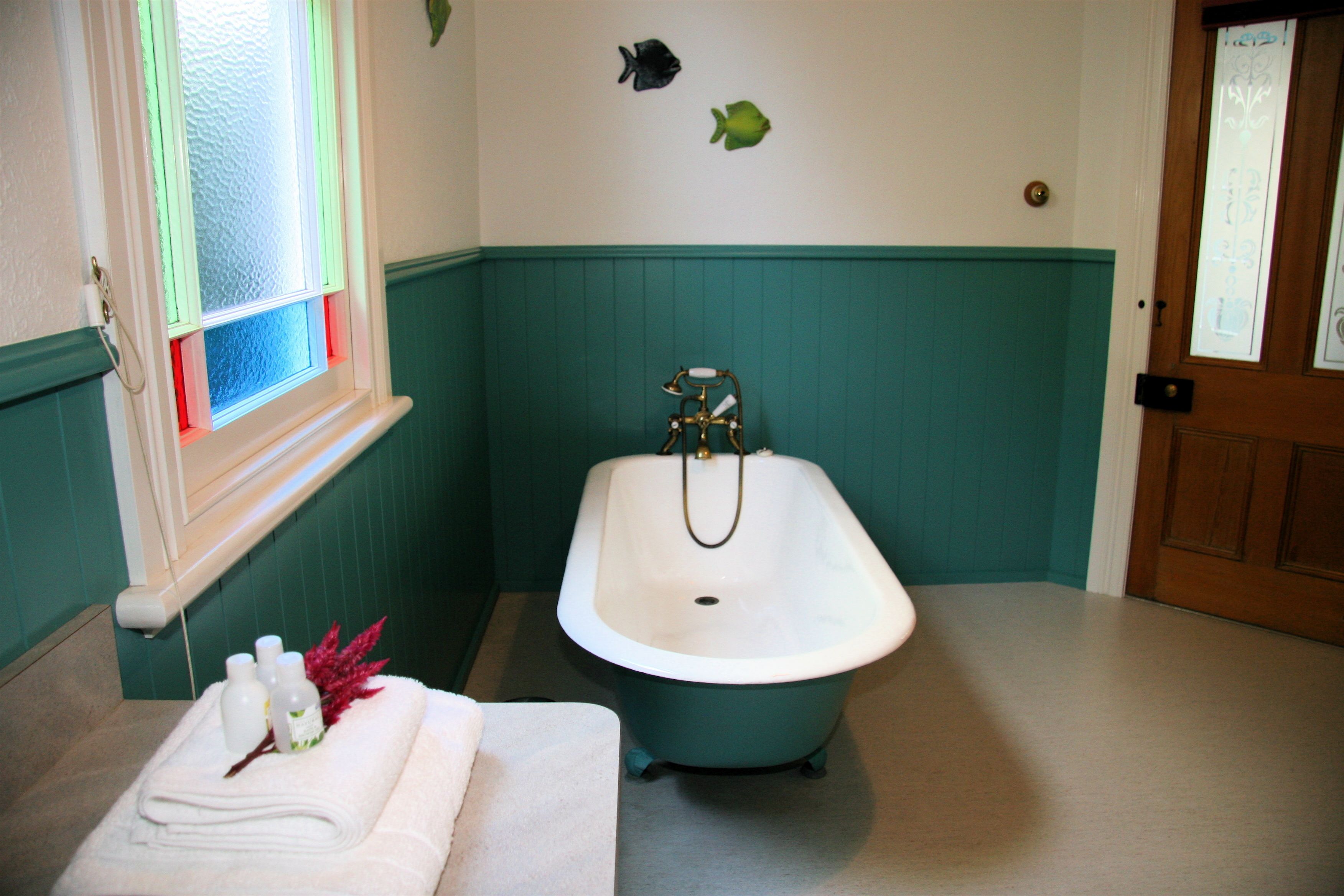 A bathroom with a freestanding bathtub, a window with frosted glass, and a towel rack with towels and toiletries.