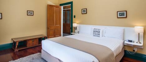 A neatly arranged bedroom with a large bed, bedside tables, a bench, and framed pictures on the walls.