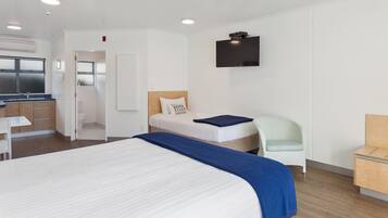 Una habitación de hotel moderna con una cama grande, un escritorio pequeño, una silla, un televisor y una kitchenette.