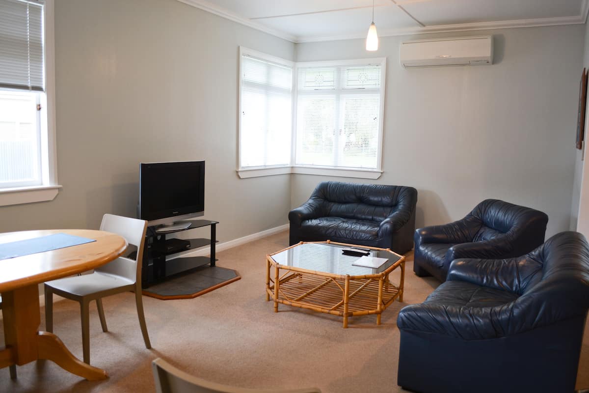 A living room with a TV, two leather sofas, a glass coffee table, and a dining table with chairs.