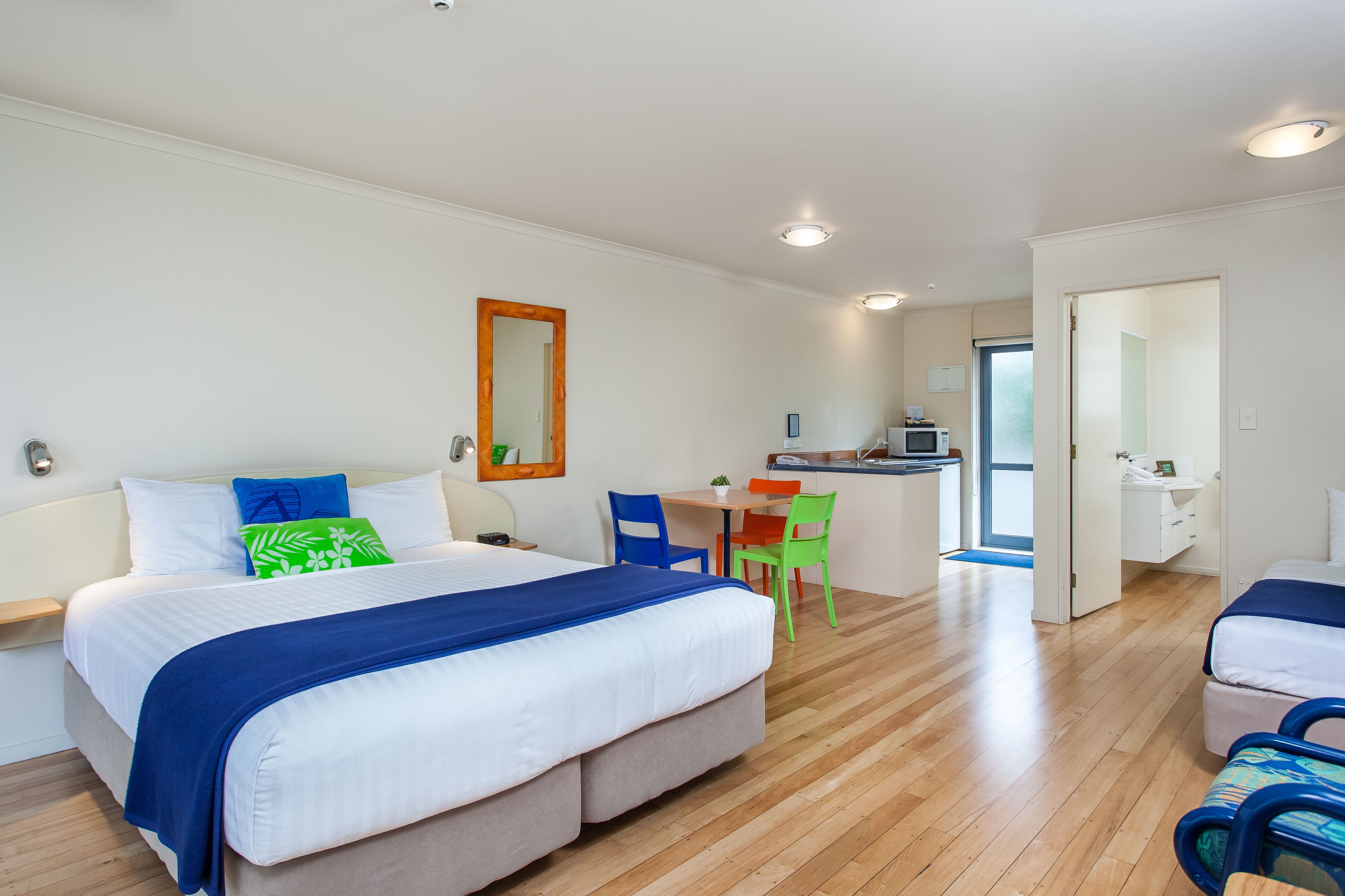 A modern hotel room with a large bed, a desk, and a kitchenette.