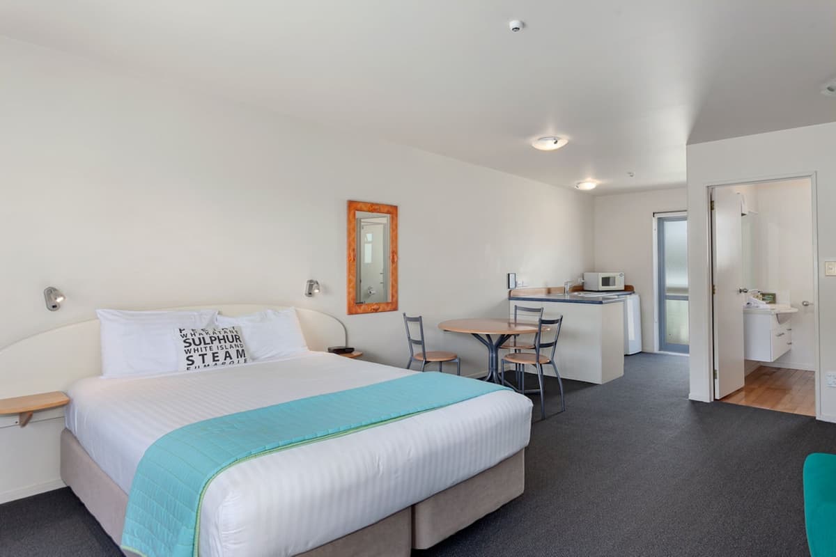 A hotel room with a bed, a desk, a chair, and a small kitchenette.