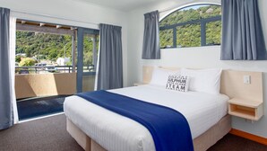 Une chambre d’hôtel avec un grand lit, une vue sur un paysage verdoyant et un balcon agrémenté de rideaux.