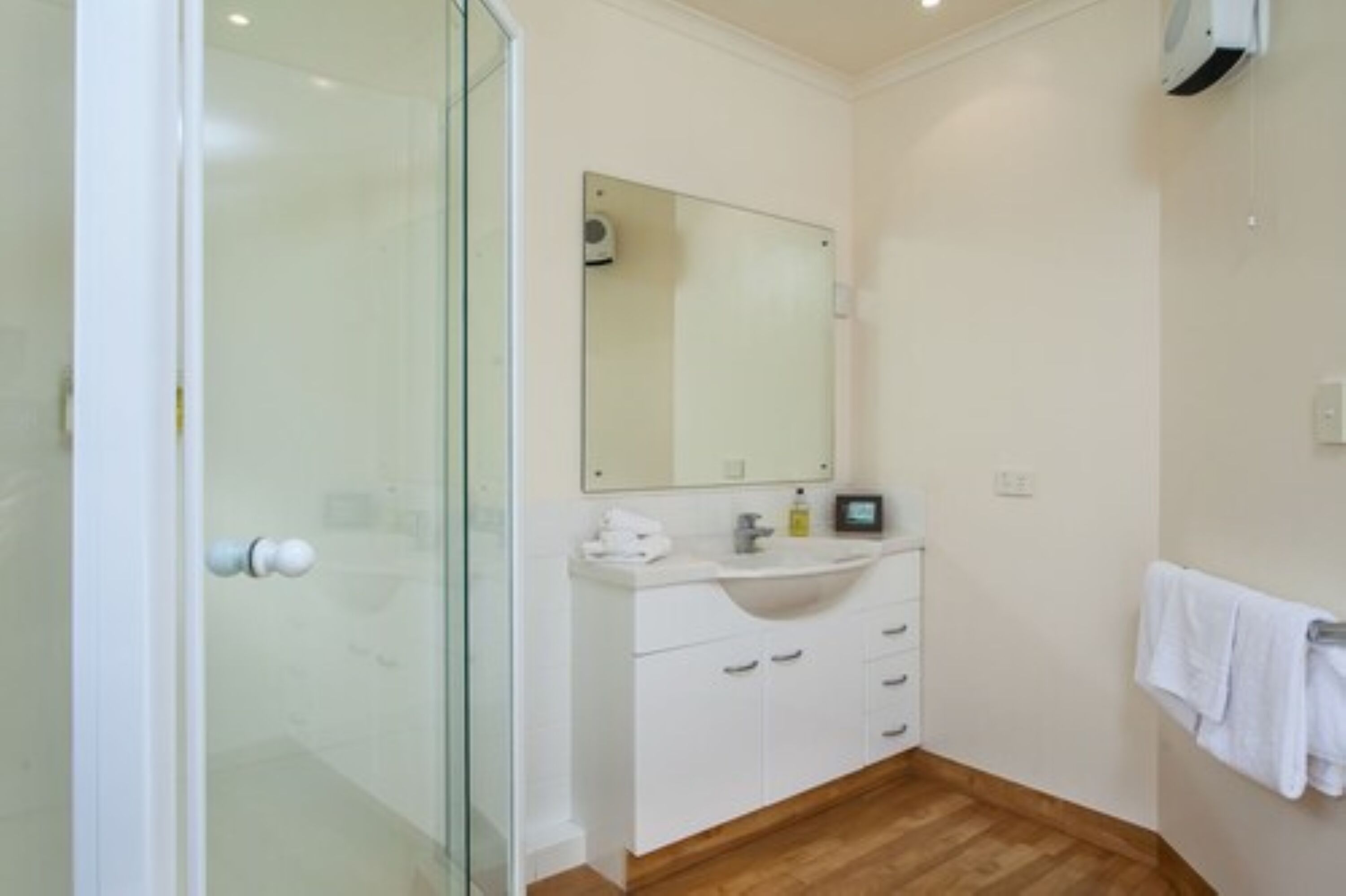 Een badkamer met een glazen douchecabine, een witte wastafel met een spiegel erboven en een handdoekhouder aan de muur.