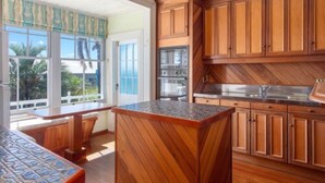 Une cuisine dotée de meubles en bois, d’un plan de travail en granit et offrant une vue sur l’extérieur grâce à de grandes fenêtres.