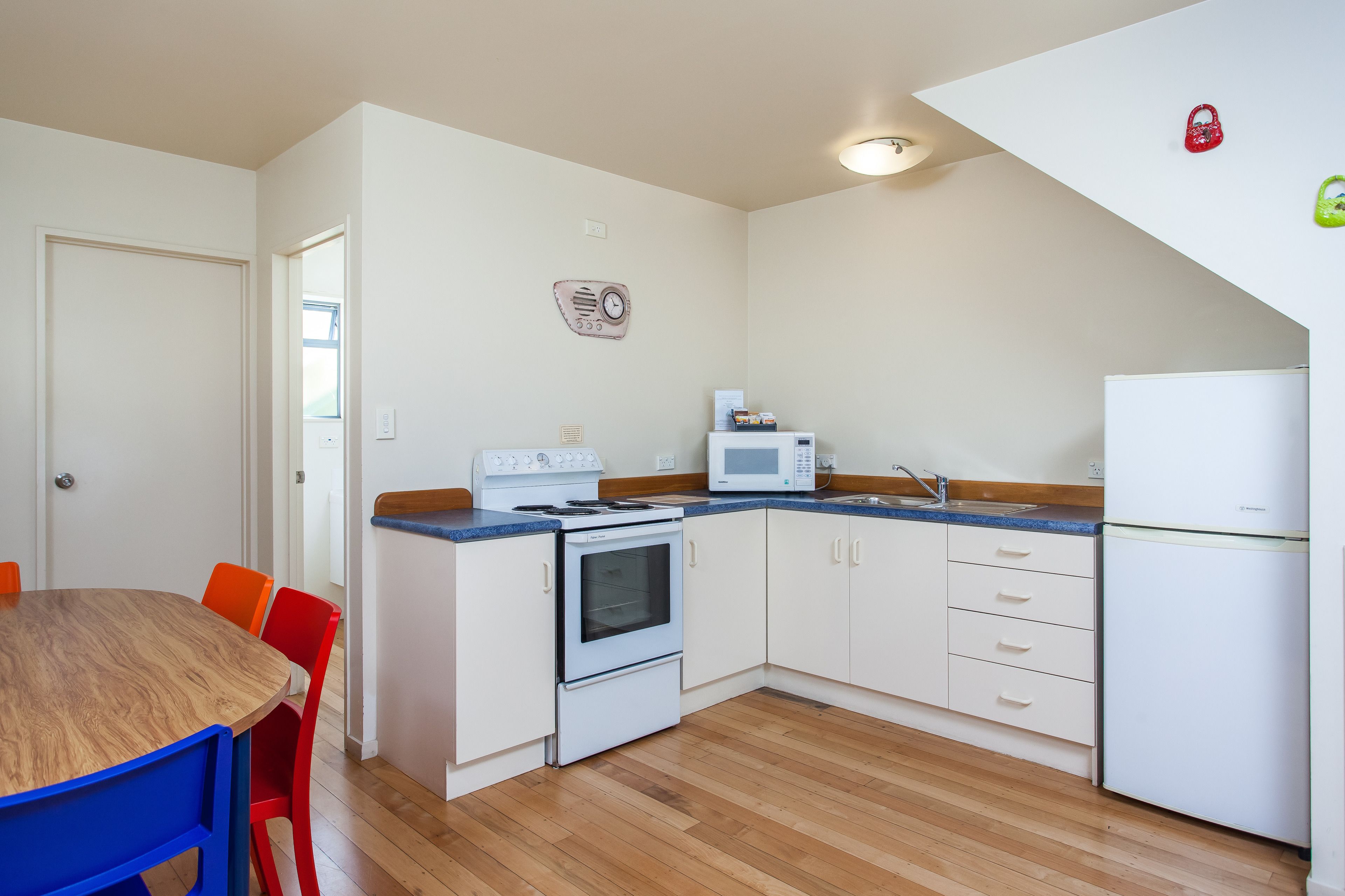 A compact kitchen with white cabinets, a microwave, a stove, and a refrigerator. There is a wooden dining table with two chairs.