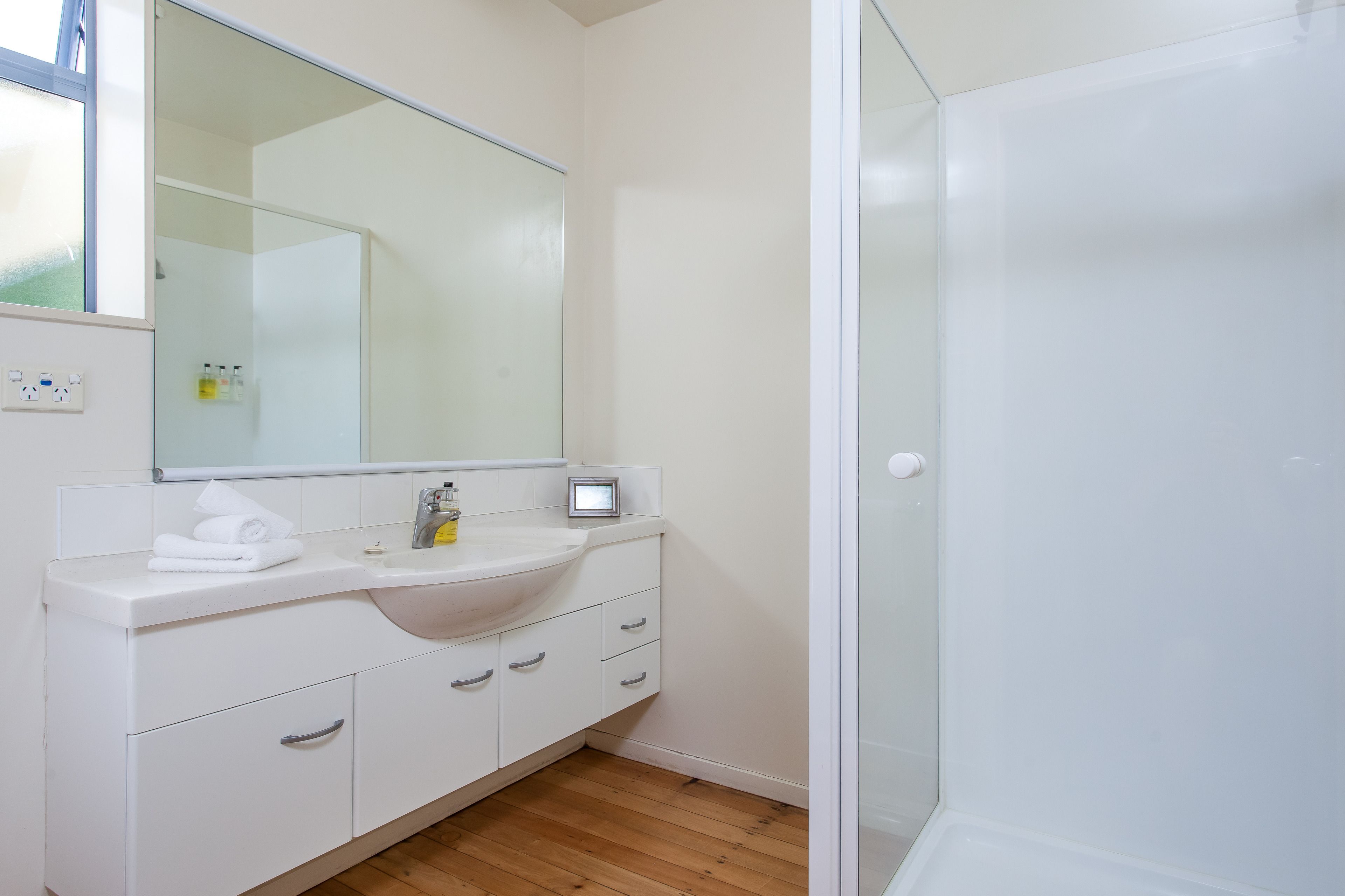 A modern bathroom with a white sink, mirror, and glass shower enclosure.