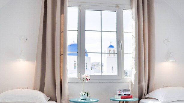 Habitación de hotel con dos camas, una ventana con vista a un edificio de cúpula azul, un florero con flores y una mesita con un libro.